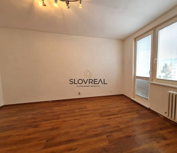 SLOVREAL - Predaj 1 - izbového bytu, Žiar nad Hronom - Interiér 1-izbového bytu s drevenou podlahou, bielymi stenami a svetlami na stropnej lampe.