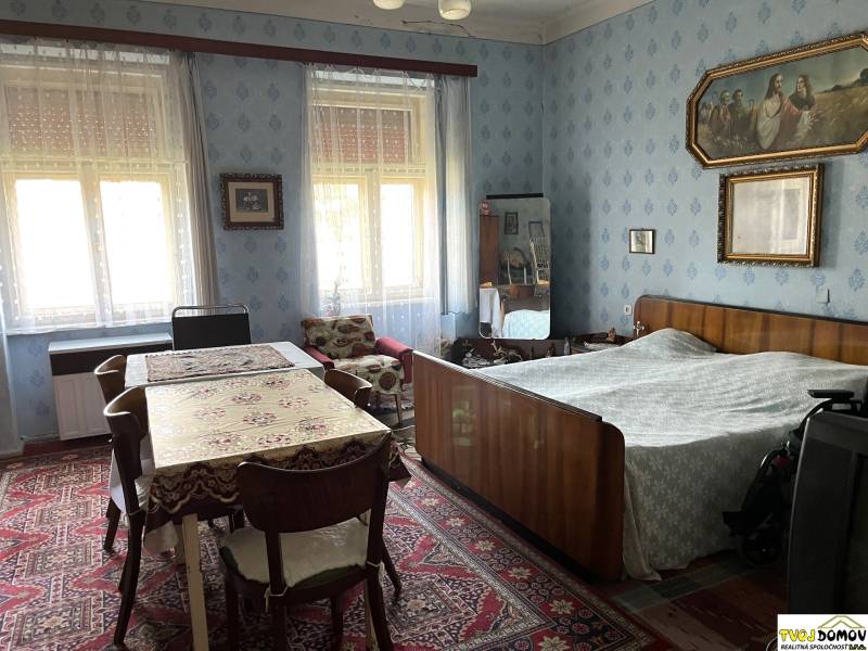 Rodinný dom v Detve na predaj - Interiér rodinného domu so spálňou, stolom, starožitným nábytkom a dekoráciami na stenách.
