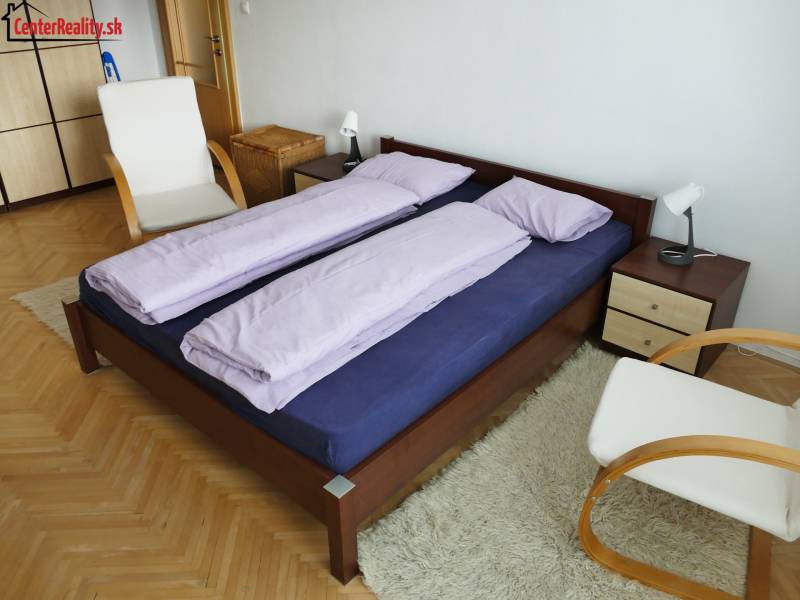 ‼️ 3 IZBOVÝ BYT NA PRENÁJOM, PARTIZÁNSKE-NÁDRAŽNÁ ULICA (ZARIADENÝ)‼️  - Spálňa v 3-izbovom byte s drevenou posteľou, stoličkou a bielym kobercom.