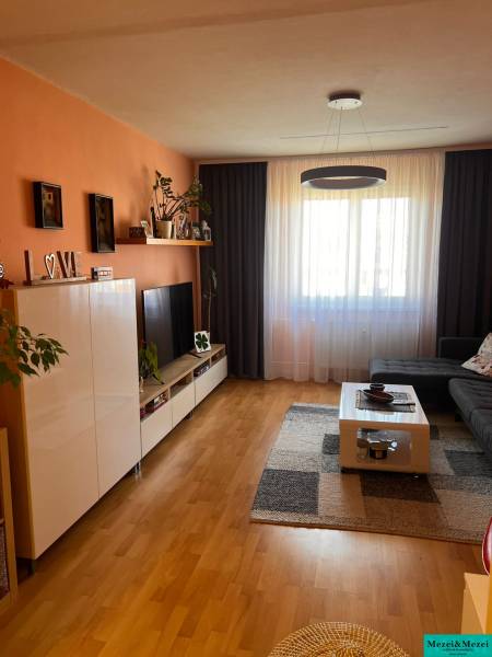 Predaj 3 izbový - Pezinok - Obývacia izba s oranžovou stenou, tmavými závesmi, veľkým oknom a nábytkom v 3-izbovom byte.