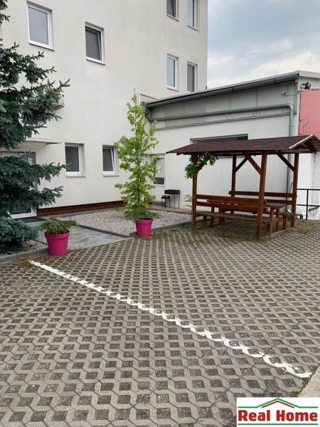 PRENÁJOM: HALA,OBCHODNÝ PRIESTOR 408 m2 v uzatvorenom areáli  - Dvorec s dlažbou, drevené sedenie a rastliny v ružových kvetináčoch na ulici Šamorínska.