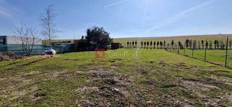 AstonReal: ponúkame na predaj pozemok o výmere 1 000 m2 - Malý Slavkov - Pozemok v Malom Slavkove obklopený stromami, pripravený na bývanie, slnečný deň.