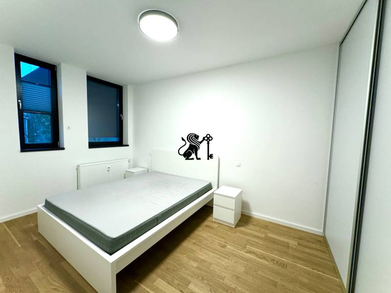 Budova s 8 apartmánmi alebo medicínske centrum, 9 park. miest- Kolibe - Spálňa s posteľou, vedľa sú dve okná, zasahuje sem umelý osvetlenie stropným svietidlom.
