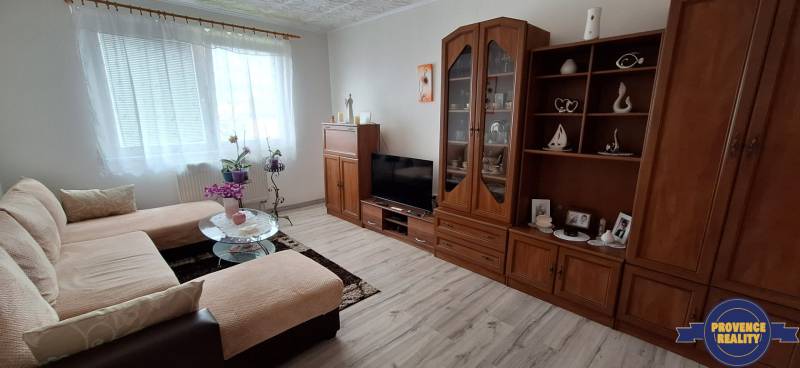 PREDAJ: 3 izbový byt s loggiou - Komárno, č. Ďulov Dvor - Obývacia izba v 3-izbovom byte s pohovkou, skrinkou a televízorom, svetlá dekorácia.