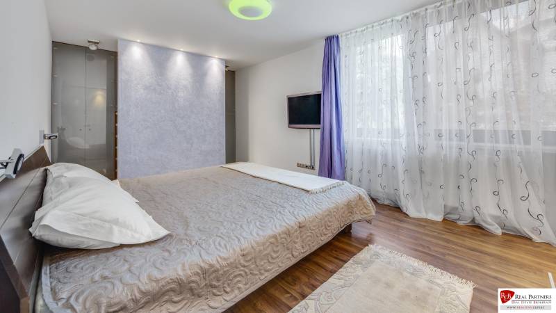 Exkluzívny 3 izbový byt, ul.Timravina, 147 m2, výhľad, parkovanie,BAI - Spálňa v 3-izbovom byte s posteľou, televíziou a pretekajúcimi závesmi na okne.