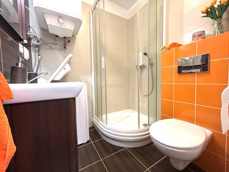 PREDAJ-GARSÓNKA-20m2-GUOTHOVA- KRAMÁRE - Kúpeľňa v garsónke s toaletou, sprchovým kútom a oranžovými obkladmi.