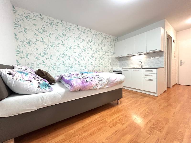 PREDAJ-GARSÓNKA-20m2-GUOTHOVA- KRAMÁRE - Garsónka s posteľou, kuchynskou linkou a kvetinovou tapetou na stene.
