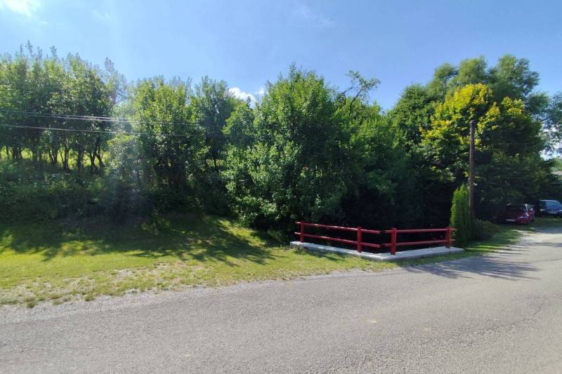 Predaj pozemku priamo v obci Hanigovce, okr. Sabinov. - Cesta obklopená zeleňou, s viditeľnými poľnohospodárskymi a lesnými pozemkami v okolí Hanigoviec.