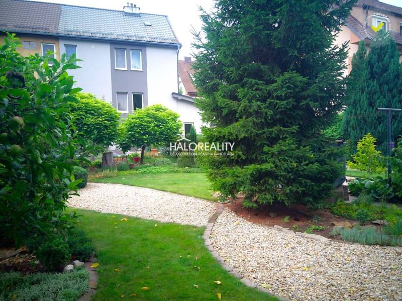Predaj, rodinný dom Nováky - EXKLUZÍVNE HALO REALITY - Krásna záhrada s chodníkom pri rodinnom dome v Novákoch, obklopená zeleňou a stromami.