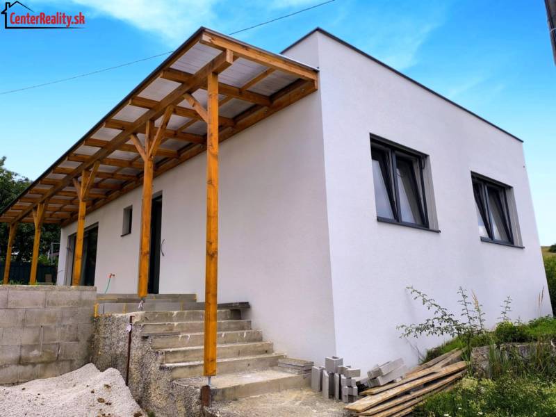 ‼️ NOVO POSTAVENÝ RODINNÝ DOM  S GARÁŽOU NA PREDAJ, MALÉ KRŠTEŇANY  ‼️ - Rodinný dom v Malých Kršteňanoch s drevenou prístavbou a betónovými schodmi, modrá obloha.
