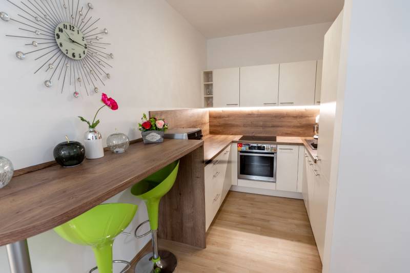 Jedinečný 3-izbový apartmán s balkónom, 71 m², Nový Ružinov - Kuchyňa s barovým stolom, zelenými stoličkami a dekoráciami v 3-izbovom byte.