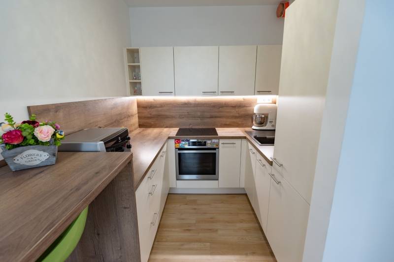 Jedinečný 3-izbový apartmán s balkónom, 71 m², Nový Ružinov - Kuchyňa v 3-izbovom byte so svetlým nábytkom a drevenou pracovnou doskou.
