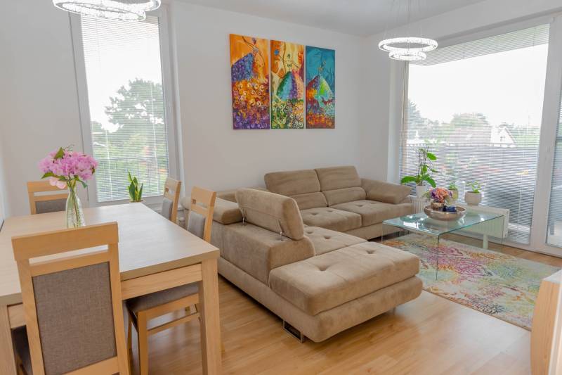 Jedinečný 3-izbový apartmán s balkónom, 71 m², Nový Ružinov - Obývacia izba s béžovou pohovkou, jedálenským stolom a farebným obrazom v 3-izbovom byte.