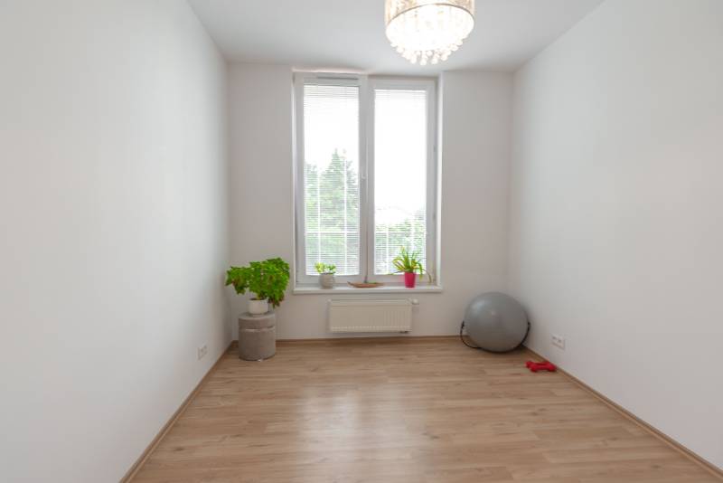 Jedinečný 3-izbový apartmán s balkónom, 71 m², Nový Ružinov - Priestranná izba v 3-izbovom byte, svetlé steny, kvetiny a fitness doplnky.