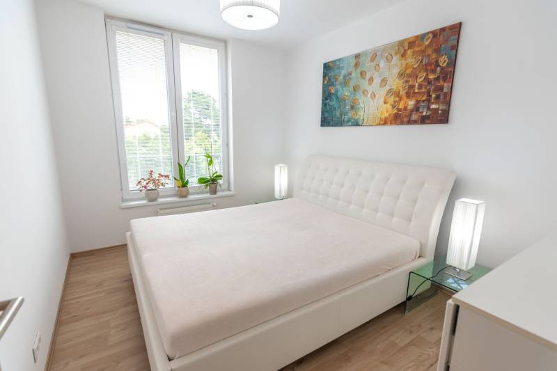 Jedinečný 3-izbový apartmán s balkónom, 71 m², Nový Ružinov - Spálňa v 3-izbovom byte s veľkou posteľou, obrazom a kvetmi na parapete.