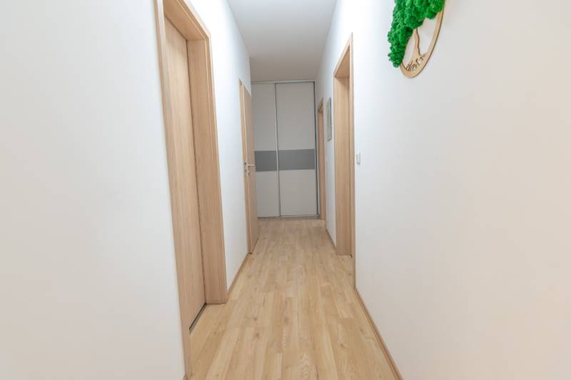 Jedinečný 3-izbový apartmán s balkónom, 71 m², Nový Ružinov - Svetlá chodba s drevenou podlahou a niekoľkými bielymi dverami v 3-izbovom byte.