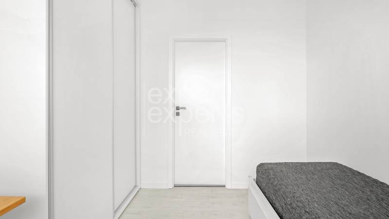 Moderný, zrekonštruovaný 3i byt 68m2, s lodžiou, pivnicou a parkovaním - Svetlá spálňa s bielym šatníkom, dreveným stolíkom a posteľou v 3-izbovom byte.