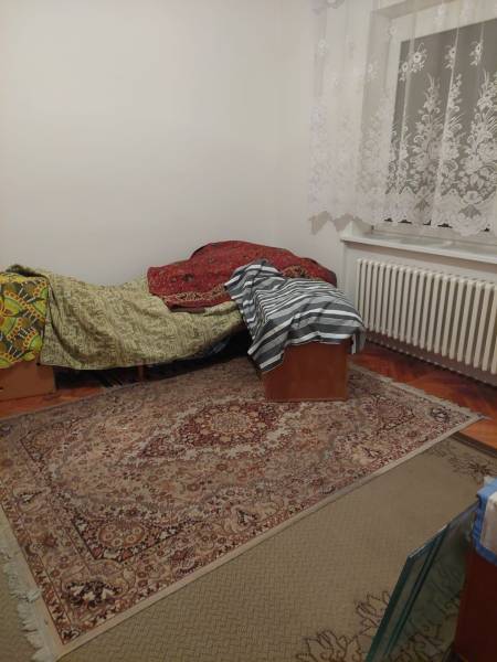 VÝNIMOČNÁ INVESTIČNÁ PRÍLEŽITOSŤ V CENTRE PIEŠŤAN - Izba v rodinnom dome s posteľou, kobercom a čipkovanými záclonami.