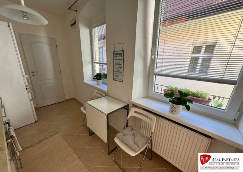 Prenájom 2-izb bytu na Ventúrskej ulici, Bratislava- centrum - Kuchyňa s oknami, stôl so stoličkami, kvetiny na parapete, 2-izbový byt.