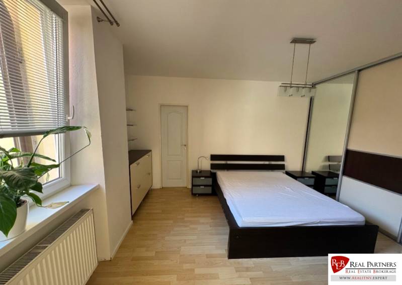 Prenájom 2-izb bytu na Ventúrskej ulici, Bratislava- centrum - Spálňa v 2-izbovom byte s posteľou, skriňou a veľkým oknom s kvetinou.