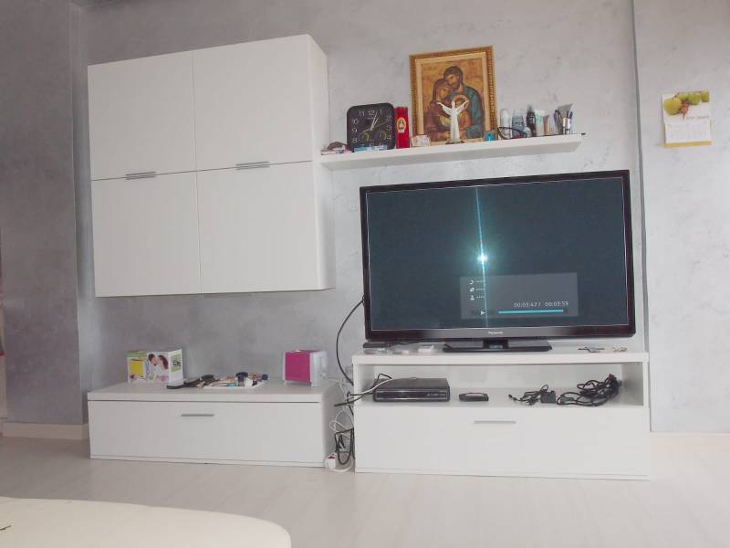 Predaj bytu 3-izbového (3+kk) s rozlohou 65 m² a terasou 10 m², Scalea - Zariadenie v 3-izbovom byte s bielymi skrinkami a televíziou na sivo maľovanej stene.