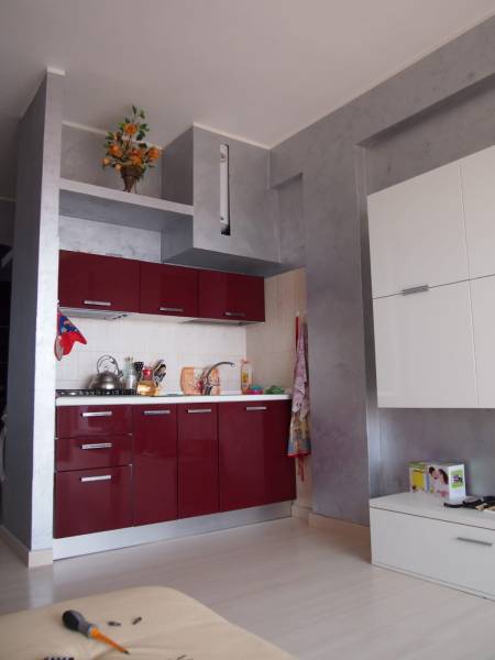 Predaj bytu 3-izbového (3+kk) s rozlohou 65 m² a terasou 10 m², Scalea - Kuchynská linka v 3-izbovom byte s lesklými červenými skrinkami a dekoráciou na poličke.