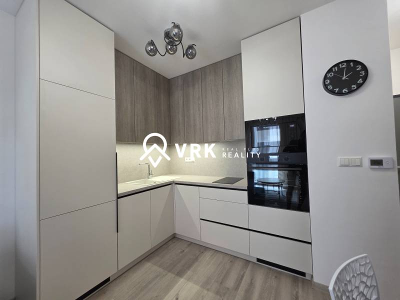 PRENÁJOM, 1.5 IZBOVÝ BYT, CÉDROVÁ UL., KOŠICE - Kuchyňa v 2-izbovom byte s bielymi a drevenými skrinkami, zabudované spotrebiče, hodiny.