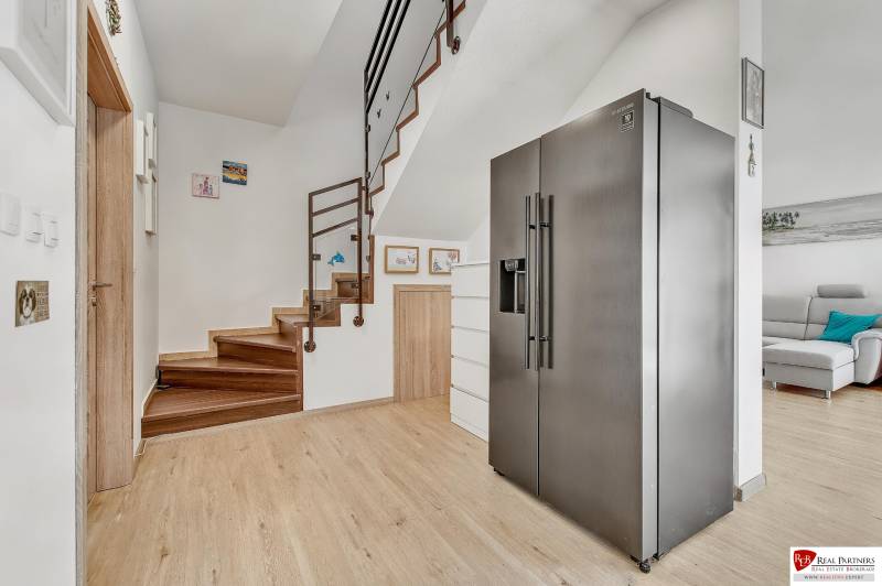 Predaj 4 izbový dom.100 m2, pozemok 208 m2, Štúrova ul, Stupava - Chladnička v chodbe rodinného domu s dreveným schodiskom a dekoráciami na stenách.