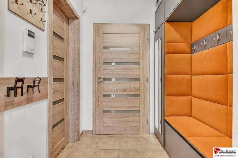 Predaj 4 izbový dom.100 m2, pozemok 208 m2, Štúrova ul, Stupava - Predsieň v rodinnom dome s oranžovou lavicou, drevenými dverami a vešiakmi na stene.