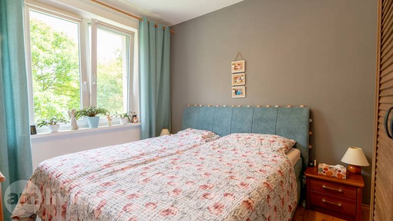 SVETLÝ – 3i s balkónom 69 m² – TOP lokalita Nová Dubnica - Spálňa s posteľou, závese v 3-izbovom byte a dreveným nočným stolíkom.