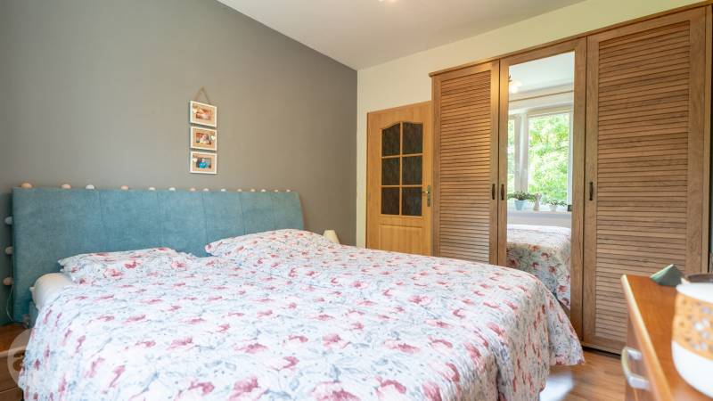 SVETLÝ – 3i s balkónom 69 m² – TOP lokalita Nová Dubnica - Spálňa v 3-izbovom byte s modrou čelovkou, drevenou skriňou a dekoráciami.