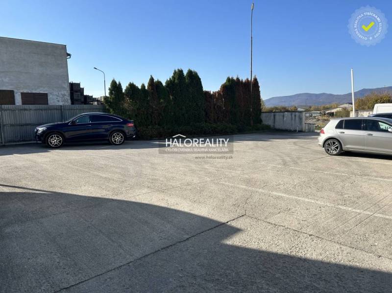 Predaj, výrobný priestor Koš, okres Prievidza - EXKL... - Parkovisko pred výrobnými priestormi, dve autá na betónovom povrchu, živý plot v pozadí.