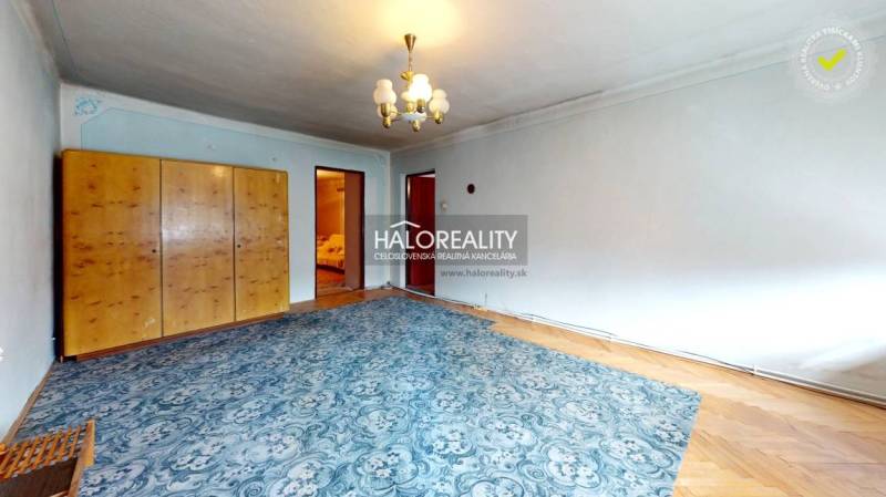 Predaj, chalupa Hrušov - EXKLUZÍVNE HALO REALITY - Izba na Chate s kobercovým kobercom, skriňou, zrkadlom a závesným svietidlom.