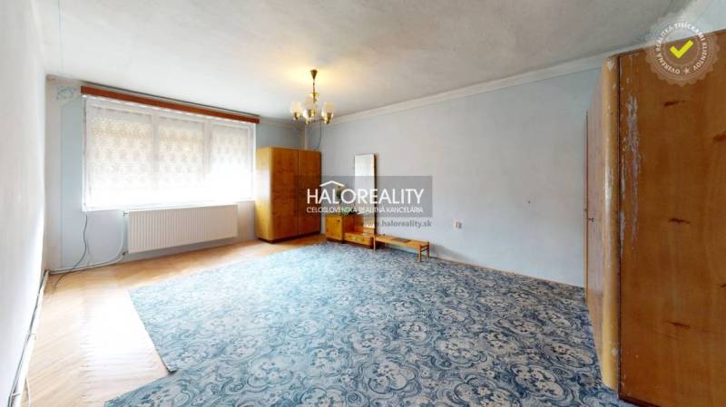 Predaj, chalupa Hrušov - EXKLUZÍVNE HALO REALITY - Interiér chaty s drevenou stenou, kachľovou pecou a jednoduchým nábytkom v útulnej miestnosti.