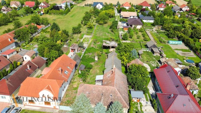 NA PREDAJ 38-ÁROVÝ STAVEBNÝ POZEMOK, BÁČ - Letecký pohľad na územie pre bývanie v Báči, obklopené zeleňou a domami.