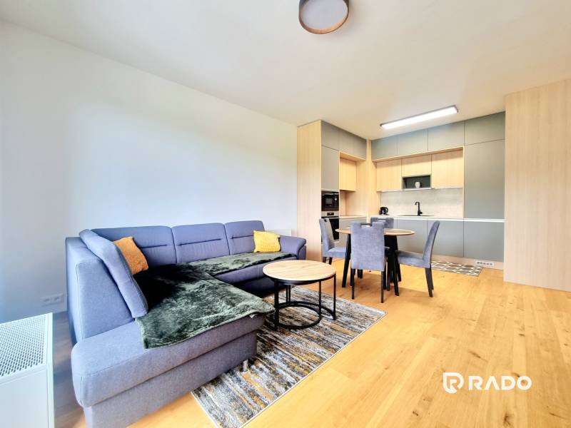 | EXKLUZÍVNE! | Krásny NOVÝ 2-izbový byt | 48m² | Čerešne - Obývacia izba s kuchyňou v 2-izbovom byte, drevená podlaha, pohodlná sedačka.