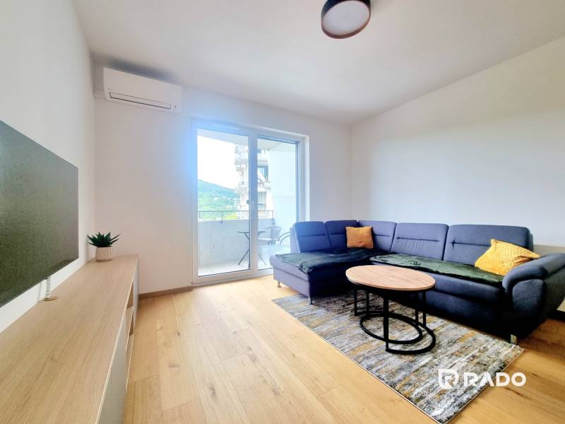 | EXKLUZÍVNE! | Krásny NOVÝ 2-izbový byt | 48m² | Čerešne - Obývačka v 2-izbovom byte s tmavým gaučom, stolíkom a balkónom.