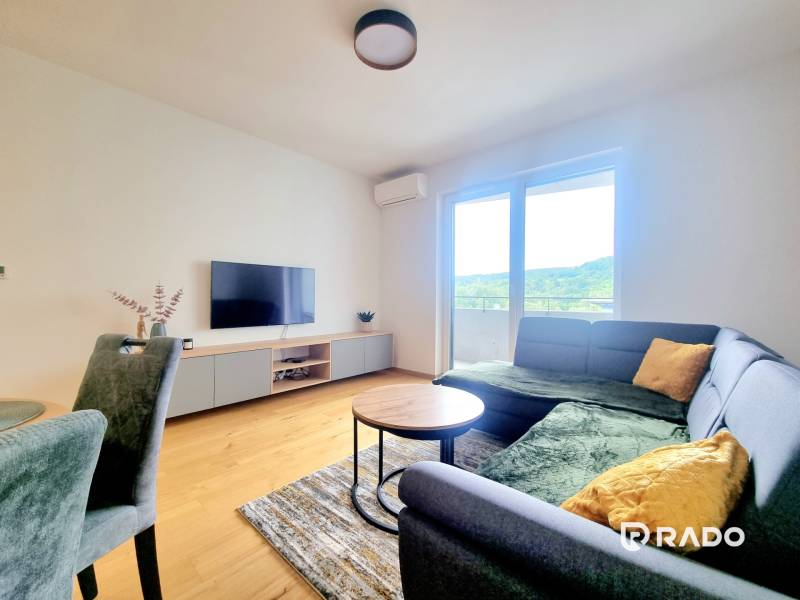 | EXKLUZÍVNE! | Krásny NOVÝ 2-izbový byt | 48m² | Čerešne - Obývacia izba v 2-izbovom byte s pohovkou, televízorom a veľkým oknom na terasu.