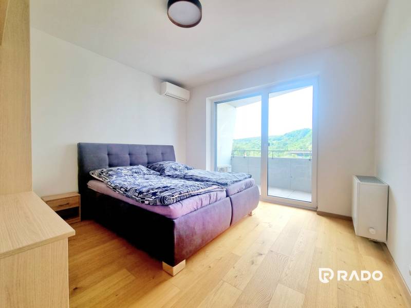 | EXKLUZÍVNE! | Krásny NOVÝ 2-izbový byt | 48m² | Čerešne - Spálňa v 2-izbovom byte s posteľou, balkónom a drevenou podlahou.