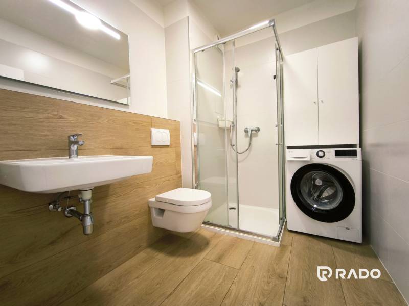 | Modedrný 1 izbový byt s parkovaním | Rovinka - Kúpeľňa v 1-izbovom byte s práčkou, sprchovým kútom a sanitou v modernej kombinácii dreva.