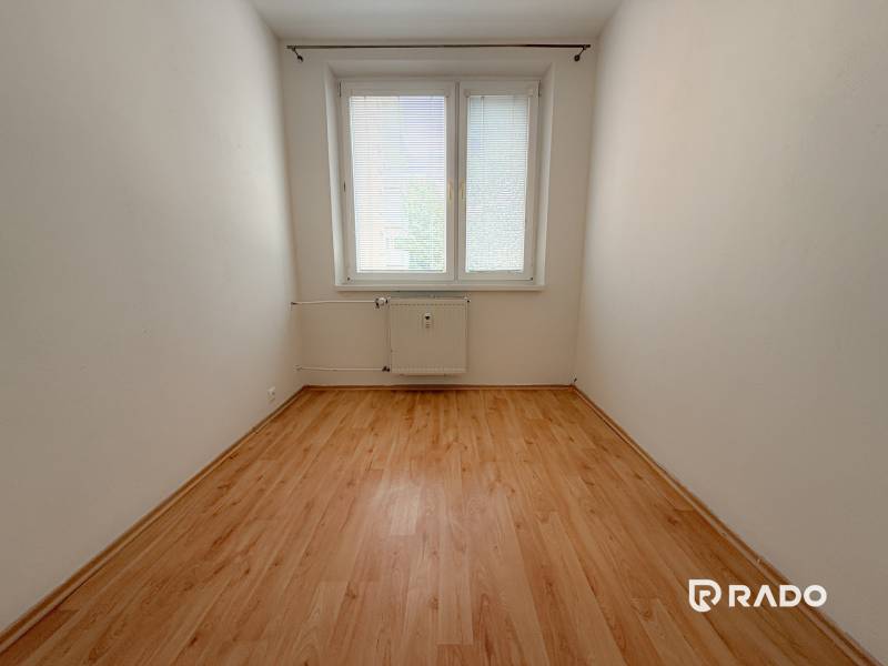 3-izbový byt, Trenčín- Juh - Prázdna izba s oknom a radiátorom, drevená podlaha, 3-izbový byt.