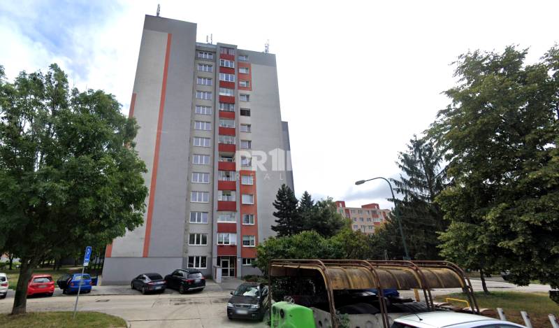 Predaj 3i byt, nepriechodné izby, výhľad, jazero Dražiak, Petržalka - Bytový dom na Krásnohorskej v Bratislave - Petržalka so zaparkovanými autami a stromami.