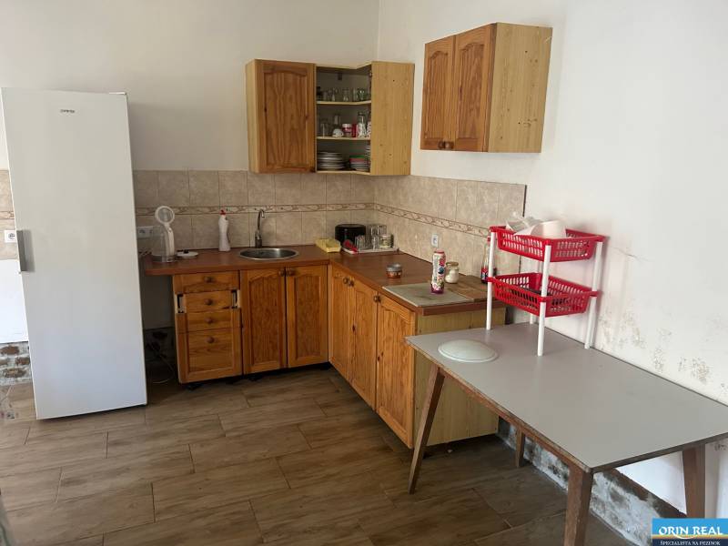 PREDAJ DOMU V ŠTEFANOVEJ S VEĽKÝM POZEMKOM - 2 399 m2 - Kuchyňa v rodinnom dome s dreveným nábytkom, chladničkou a stolom s plastovými košíkmi.