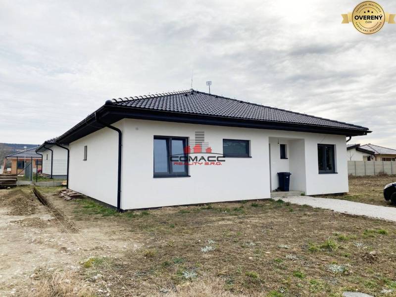 Výstavba inteligentného 4 izbového bungalovu v NM a okolí - Rodinný dom na ulici v Novom Meste nad Váhom s bielou fasádou a tmavou strechou.