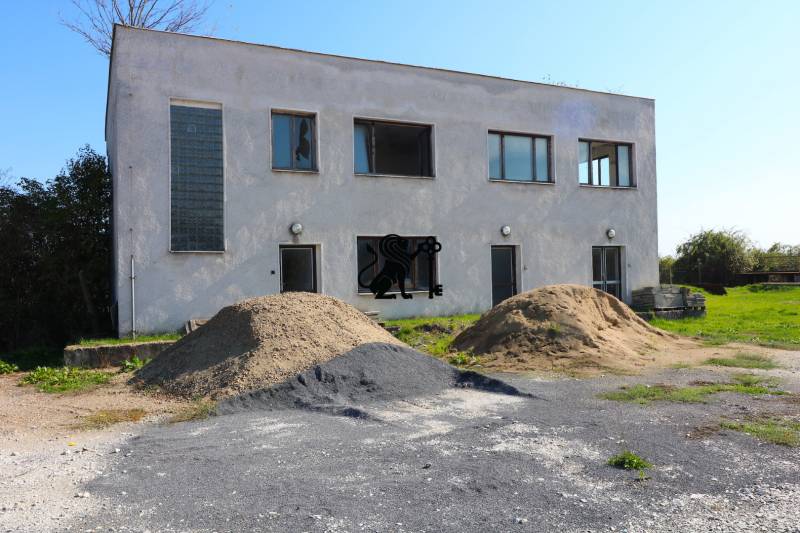 Na predaj sklady v obci Chrastince, Veľký Krtíš - Dvojpodlažná budova so štyrmi oknami a kopami štrku na ulici Chrastince.