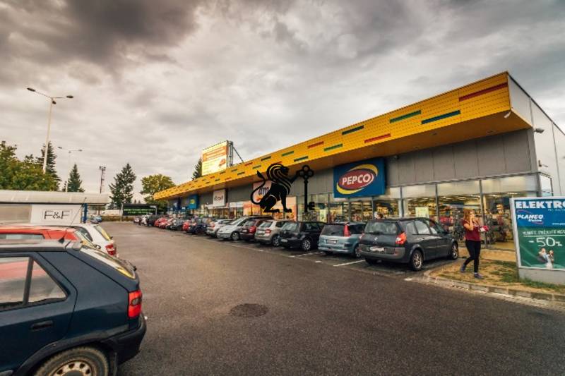 Obchodné priestory na prenájom v nákupnom centre RGB Javorina - Obchodné priestory na ulici Trenčianska, automobily zaparkované pred obchodmi, zákazníci nakupujú.