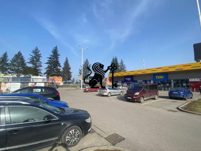 Obchodné priestory na prenájom v nákupnom centre RGB Javorina - Parkovisko pri obchodných priestoroch na ulici Trenčianska s autami a stromami v pozadí.