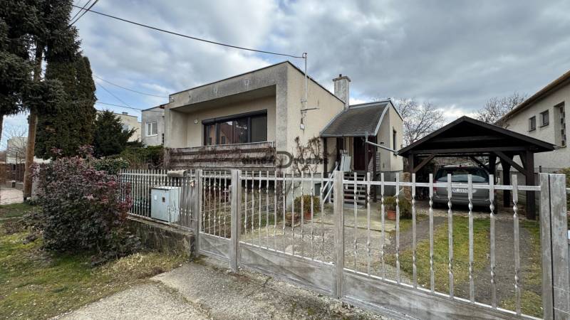 NA PREDAJ rodinný dom v Jelšovciach - EXKLUZÍVNE - Rodinný dom so záhradou, oplotením, dreveným prístreškom a bránou, v pochmúrnom počasí.