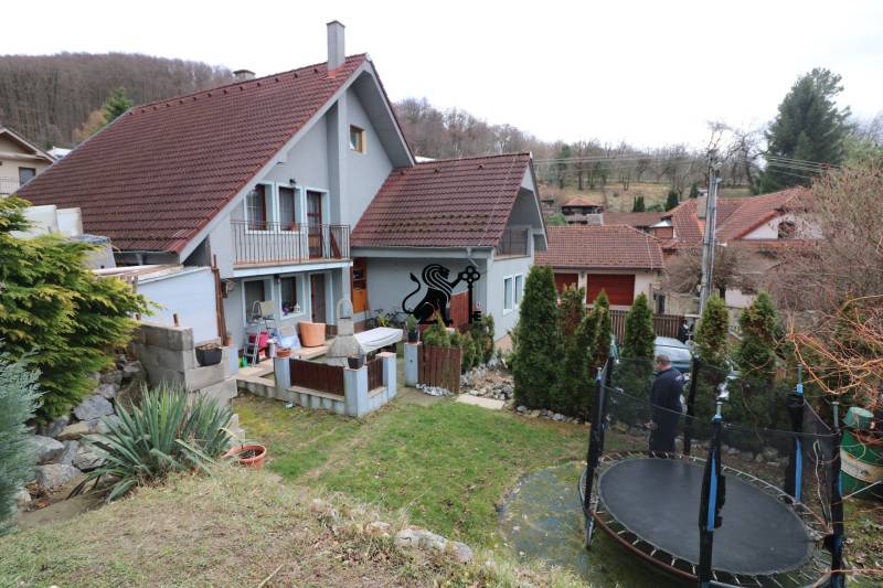 ZNÍŽENÁ cena-viacgeneračný  rodinný dom v Borinke - Rodinný dom s červenou strechou na ulici Borinka, zahrada, trampolína, stromy, kopce v pozadí.
