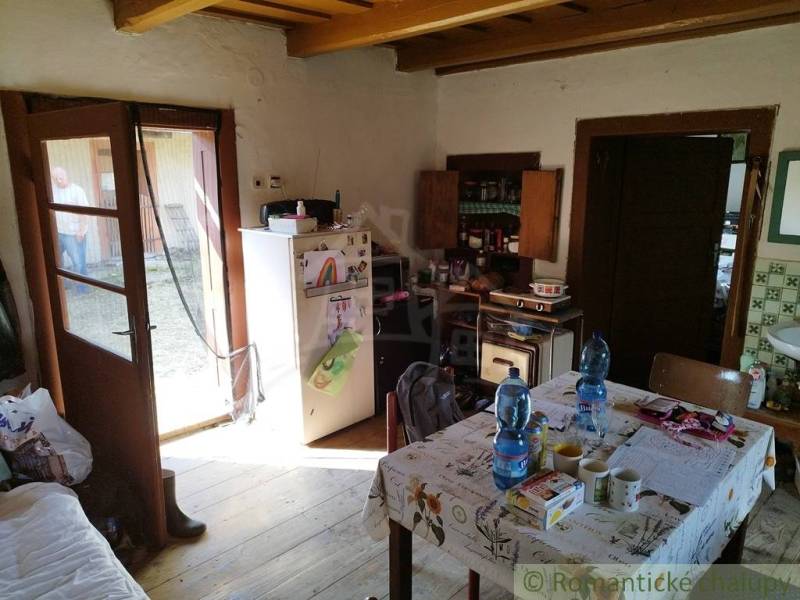 Veľký, vyše 4,5Ha slnečný pozemok s chalupou v strede, na lazoch, pri  - Kuchyňa na chate s dreveným dekorom, stolom so základnými potrebami a dverami do záhrady.